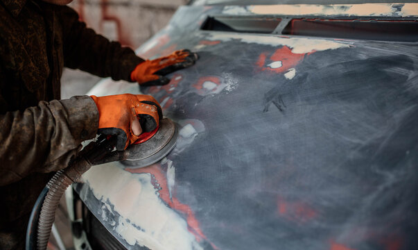 grinds a car putty, preparing a body for painting, car body repair.