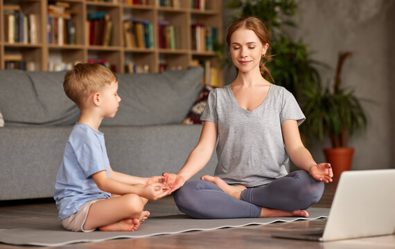 Mom With Child Little Son Doing Yoga Online, Sitting In Lotus Pose On Floor And Meditating With Closed Eyes