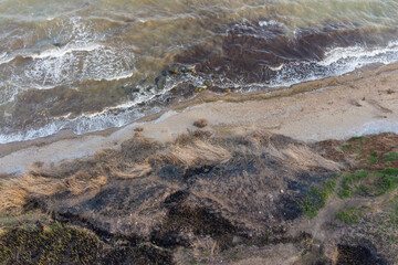 Steep sea shore and surf. Sea water muddy with sand after storm and algae. Aerial view.