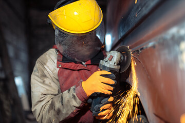 man in a helmet grinds metal with a grinder, car body repair.