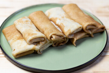 Row of filled pancakes laying on green plate on wooden table