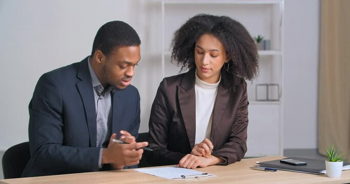 Two afro american business partners couple of ethnic people sitting at table reading document woman advisor lawyer consultant showing to employee contract paper cooperation agreement offers to sign