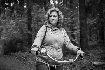 Naklejka na ściany i meble A blonde woman walks through the forest with a bicycle. Black and whait photo.