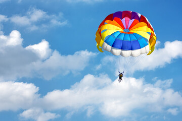 Paragliding using a parachute on background of blue cloudy sky.