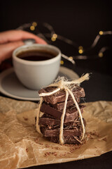 Stacked chocolate bars with cup. Dark chocolate on parchment paper tied with twine on black. Dark chocolate, cup and garland.