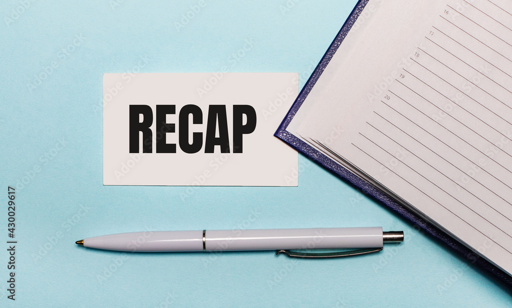 Poster on a light blue background, an open notebook, a white pen and a card with the text recap. view from 