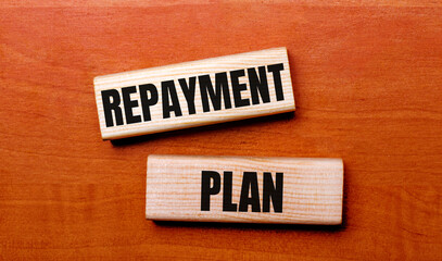 On a wooden table are two wooden blocks with the text question REPAYMENT PLAN