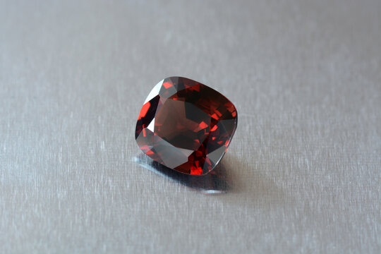 Natural deep red color cushion cut faceted loose spinel genuine gemstone. Daylight from window. Satin shine polished aluminium background surface.