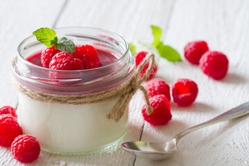Delicious dessert panna cotta with raspberry sauce, fresh raspberries and mint on white wooden background