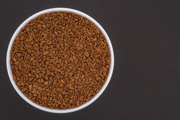 White glass bowl of instant coffee. Isolated on a dark grey background. Top view close up photo.