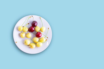 A group of yellow and red cherries on a plate. Isolated on a blue background. Sweet cherry