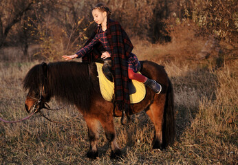 Little girl plays with horse in forest. Girl feeding apples to ponies outdoors. 