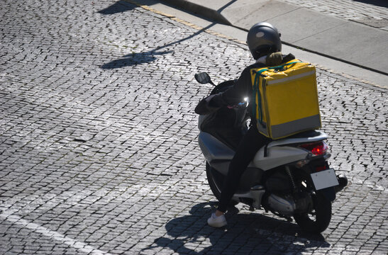 Estafeta de entregas de refei&ccedil;&otilde;es por aplica&ccedil;&atilde;o, numa scooter com mochila t&eacute;rmica &aacute;s costas, parado numa passadeira para pe&otilde;es