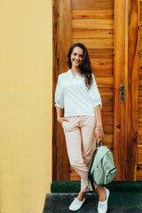 stylish girl in a white blouse, cream-colored trousers, white sneakers and with a green backpack