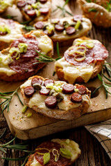 Grilled bruschetta  with cheese, sausage and herbs on a wooden board, close-up view. Party food idea