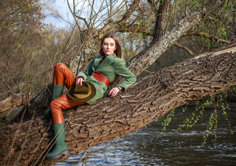 Beautiful lady in rustic style clothes on tree by the river