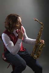 Full-length studio portrait of a young musician guy holding a saxophone.