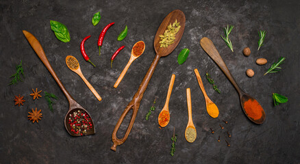 Variety of spices in wooden spoons on black background.