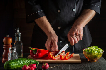 Close-up of a chef or cook hands cutting peppers on cutting board. Professional preparation of salad in the kitchen in a restaurant or cafe