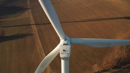 Close up a large spinning wind turbine on the background of wind farm at sunset.  - Powered by Adobe