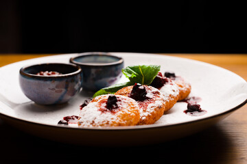 Side view photo of some cheese pancakes with some jelly and sour cream.