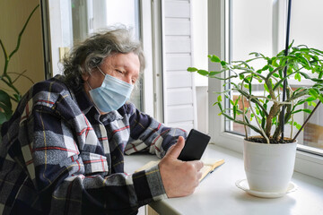 An elderly man in a protective mask on self-isolation speaks by phone via video link