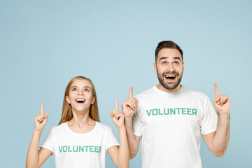 Two young friends couple teen girl man wears white t-shirt green title volunteer point advert isolated on pastel blue color background. Voluntary free team work assistance help charity grace concept.