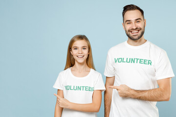 Two young friends couple teen girl man wears white t-shirt green title volunteer point advert isolated on pastel blue color background. Voluntary free team work assistance help charity grace concept.