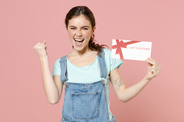 Young overjoyed caucasian woman 20s in trendy denim clothes blue t-shirt hold gift voucher flyer...