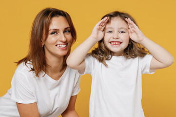 Fototapeta na wymiar Happy woman in white t-shirt have fun with cute child baby girl 5-6 years old cover face. Mommy little kid daughter isolated on yellow orange color background studio. Mother's Day love family concept.