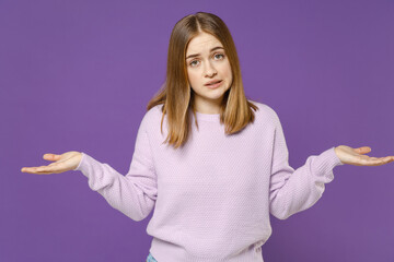 Young confused mistaken sad student woman 20s in purple knitted sweater point index finger aside scream shout spread hands isolated on violet color background studio portrait People lifestyle concept.