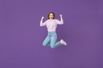Full length young excited overjoyed happy woman 20s wearing purple knitted sweater jump high do winner gesture clench fist isolated on violet color background studio portrait People lifestyle concept.