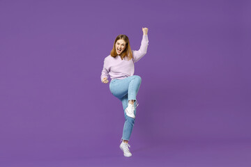 Full length young overjoyed happy student caucasian woman 20s in purple sweater do winner gesture clench fist with raised up leg isolated on violet background studio portrait People lifestyle concept.