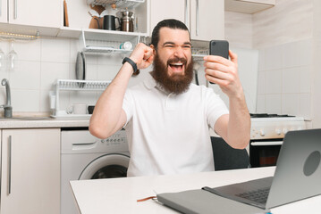 Yay, I have got it. Bearded man is joyful about he sees on his smartphone.
