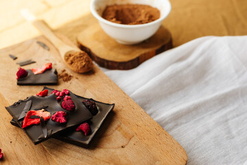  Chocolate bar with strawberries on wooden board with white bowl with cocoa powder and wooden spoon