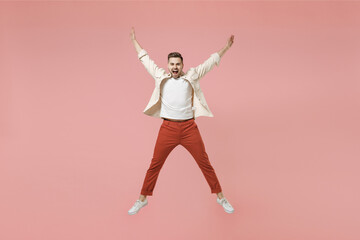 Full length young smiling excited overjoyed joyful fun trendy fashionable caucasian man in jacket white t-shirt jump high with outstretched hands isolated on pastel pink background studio portrait