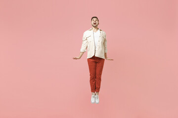 Full length young smiling happy overjoyed joyful fun trendy fashionable caucasian excited man 20s wear jacket white t-shirt jump high fly isolated on pastel pink color background studio portrait