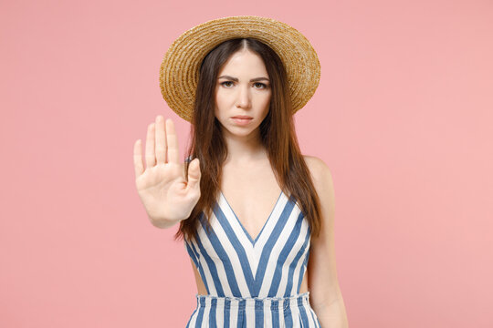 Young Serious Strict Caucasian Woman In Summer Clothes Dress Straw Hat Do Stop Palm Gesture Look Camera Refusing Say No Isolated On Pastel Pink Background Studio Portrait. People Lifestyle Concept