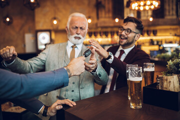  Three business people celebrating successfully done job at restaurant. One man taking car key from his drunk business partner.