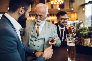  Three business people celebrating successfully done job at restaurant. One man taking car key from his drunk business partner.
