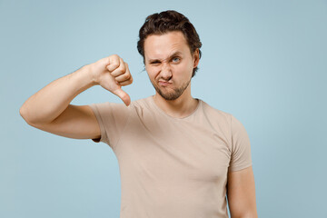 Young displeased sad man in casual basic beige blank print design t-shirt looking camera show thumb...
