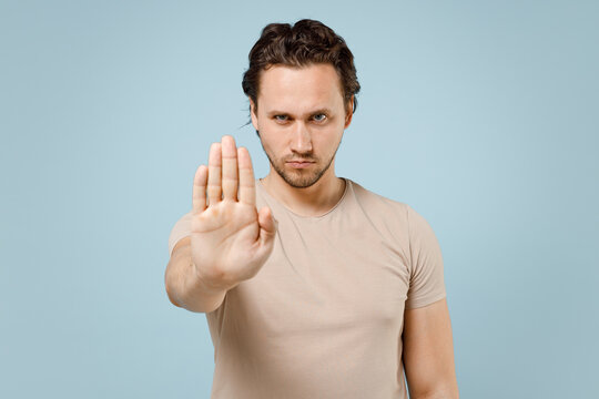 Young sad angry strit caucasian man 20s in casual basic beige t-shirt point index finger aside scream shout do it isolated on pastel blue color background studio portrait. People lifestyle concept