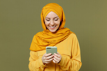 Smiling young arabian asian muslim woman 20s in abaya hijab yellow clothes hold in hand using...