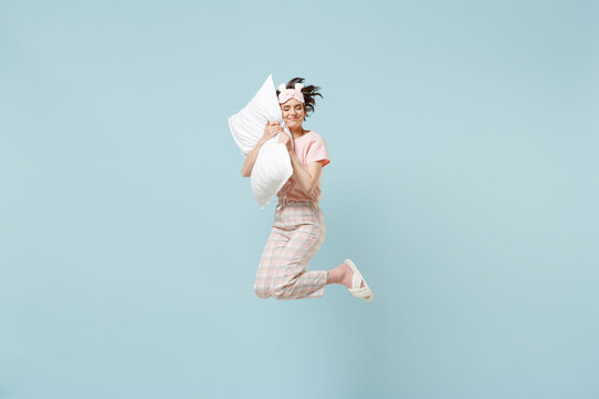 Full length young sleeping happy woman 20s wear pajamas jam sleep eye mask rest relaxing at home jump high sleep on pillow isolated on pastel blue background studio. Good mood night bedtime concept.