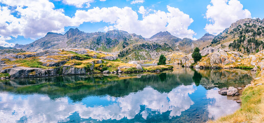Fototapeta na wymiar Panoramic view of mountainous landscape reflected in a lake with a beautiful mountains on a sunny summer day. Concept of mountain trip. Circo Saboredo, Aran Valley, Pyrenees, Catalonia, Spain.