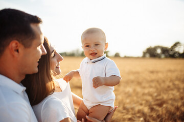 Happy parents hold a child in their arms in a wheat field. A woman and a man play with a child on a sunny summer day. Photo of a happy family.