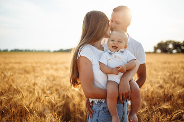 Joyful parents hold a baby in their arms in a wheat field. Family in white t-shirts on a sunny day. A man and a woman with a child in their arms.