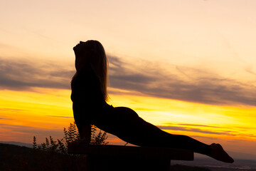Naklejka na ściany i meble Silhouette of a young woman doing cobra pose at sunset