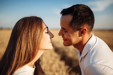 Fototapeta premium Portrait of a happy boy and girl on the background of a ripe field with wheat. A loving couple smiling to each other on a sunny day. Man and woman in the summer in a wheat field.