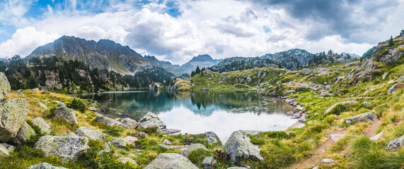Fototapeta na wymiar Panoramic view of mountain lake surrounded by mountains reflected in the water. Concept of mountain trip, summer vacations and nature. Circo Saboredo, Aran Valley-Pyrenees, Catalonia, Spain.